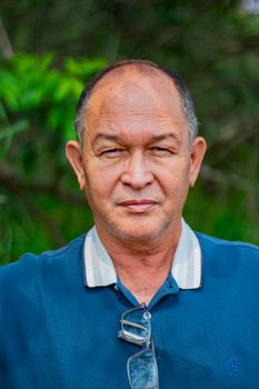 Portrait of a senior man wearing a blue polo shirt in a natural outdoor setting.