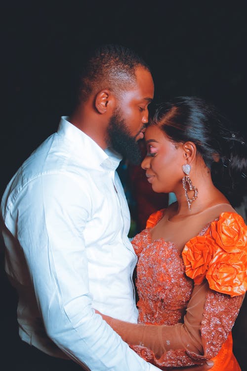 Man in White Long Sleeve Shirt Kissing a Woman on Forehead