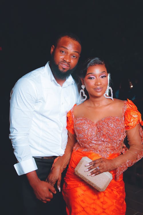 Bearded Man in White Long Sleeves Shirt Standing Beside Woman in Orange Gown