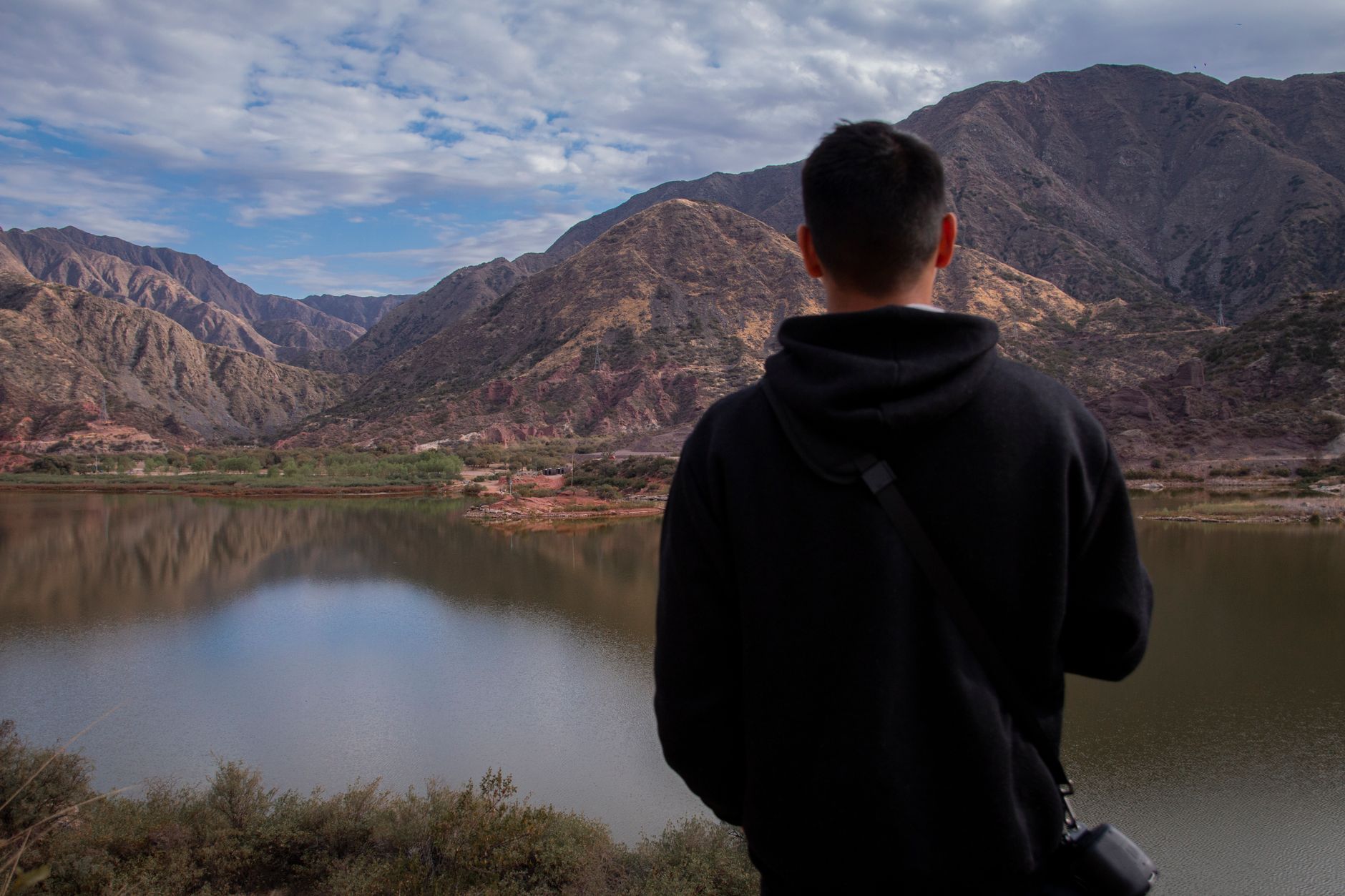 A man stands by a tranquil lake in La Rioja, Argentina, gazing at the majestic mountains.
