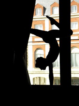 A dramatic silhouette of a gymnast in a handstand pose by a large window, inspiring strength and grace.
