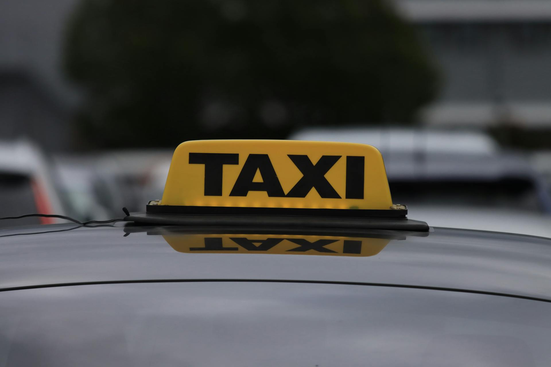 Yellow taxi sign on a car roof in a city parking area during daylight.