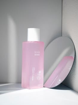 Elegant pink toner bottle reflects in a minimalist setup featuring soft shadows and muted tones.