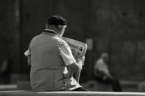 Free Black and white image of an elderly man reading a newspaper outdoors in Turin, Italy. Stock Photo