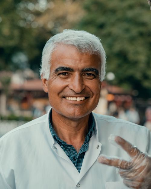 Free Close-up of a smiling elderly man outdoors with peace sign gesture. Stock Photo