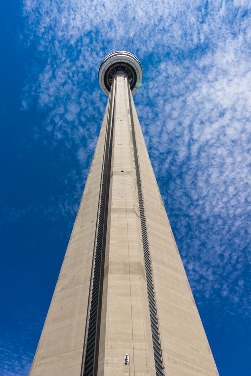 Free A striking low-angle view of the iconic CN Tower reaching into a bright blue sky with scattered clouds. Stock Photo