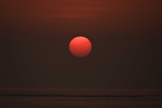 Dramatic sunset over the ocean with a fiery sun and vibrant sky.