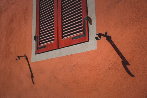 Free Close-up of an orange wall featuring a wooden shutter casting dramatic shadows. Stock Photo