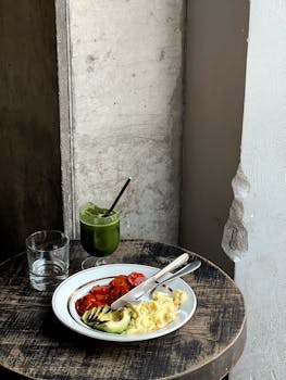 A rustic breakfast setting featuring avocado, scrambled eggs, and tomatoes paired with green juice.