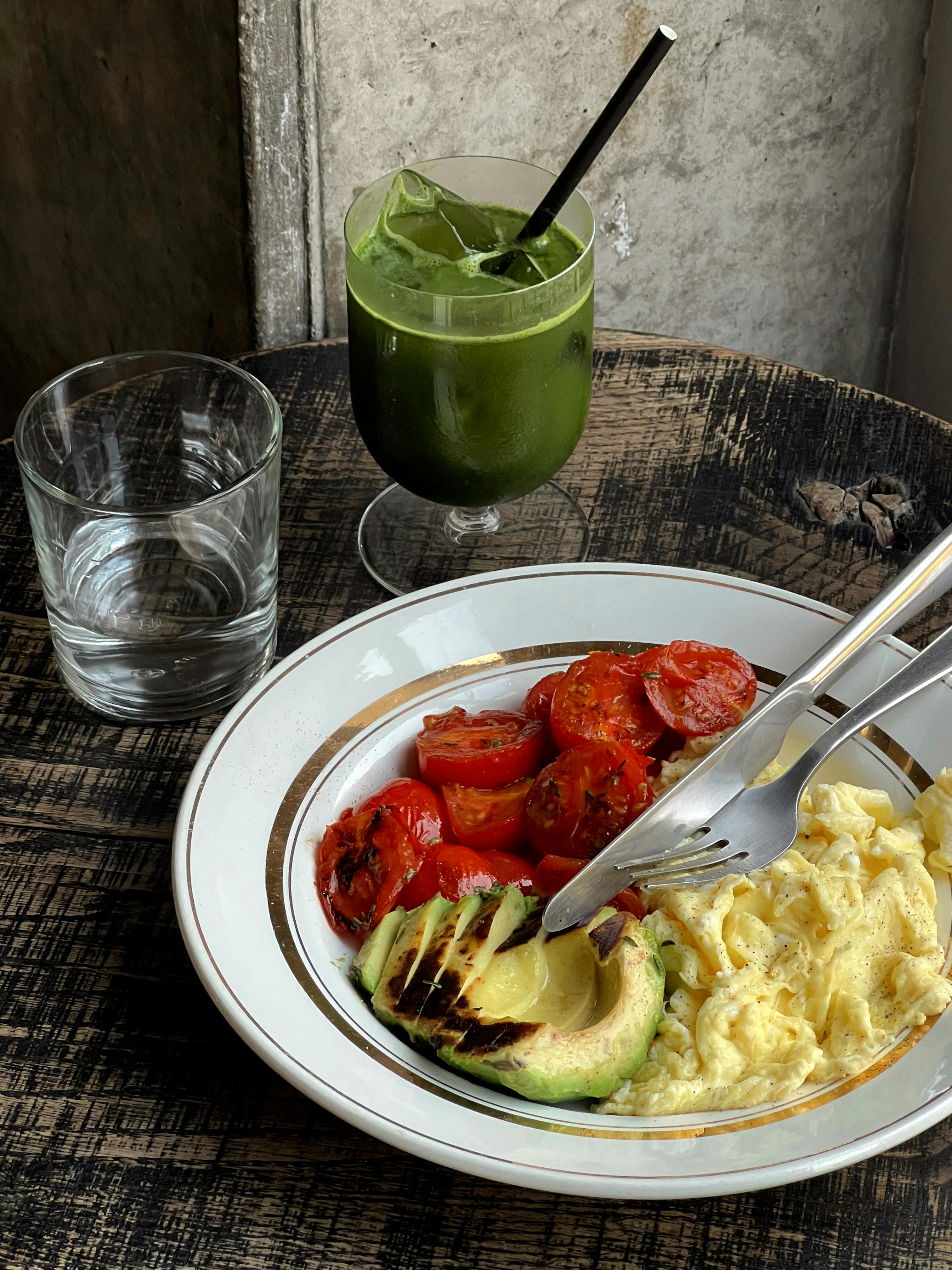 Scrambled eggs with avocado and tomatoes, served with a green juice on a rustic table.