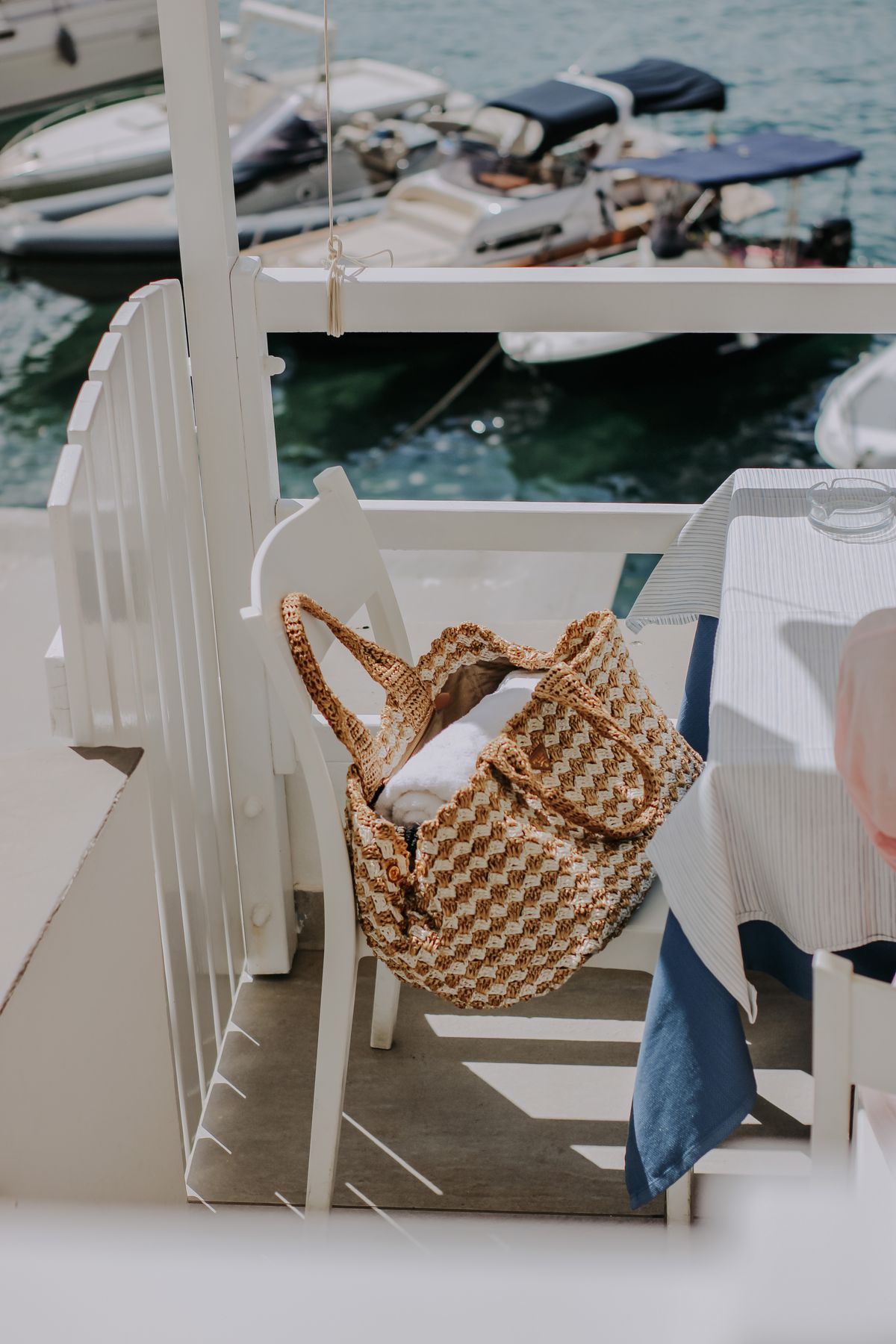 Raffia handbag resting on a chair at a harbor restaurant terrace