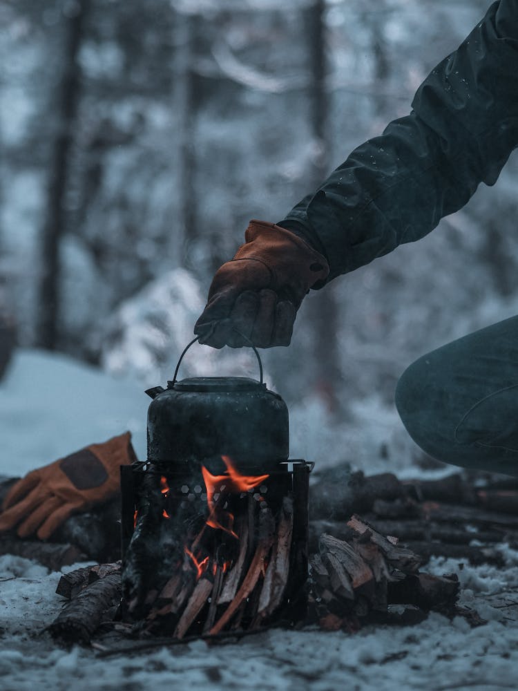 Hand In Glove Holding Kettle Over Bonfire In Winter