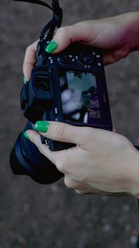 A close-up view of hands with green nails holding a DSLR camera outside.