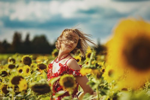 Free Girl in Red and White Floral Spaghetti Strap Top Standing on Sunflower Field Stock Photo