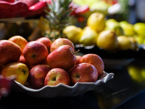 A close-up of fresh apples in a decorative plate on a table, with pears in the background.