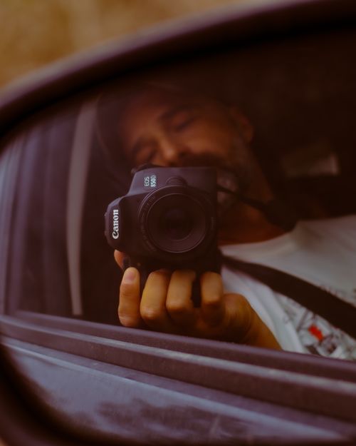 Free A man captures a photo of himself in a car's side mirror, focused on the camera lens. Stock Photo