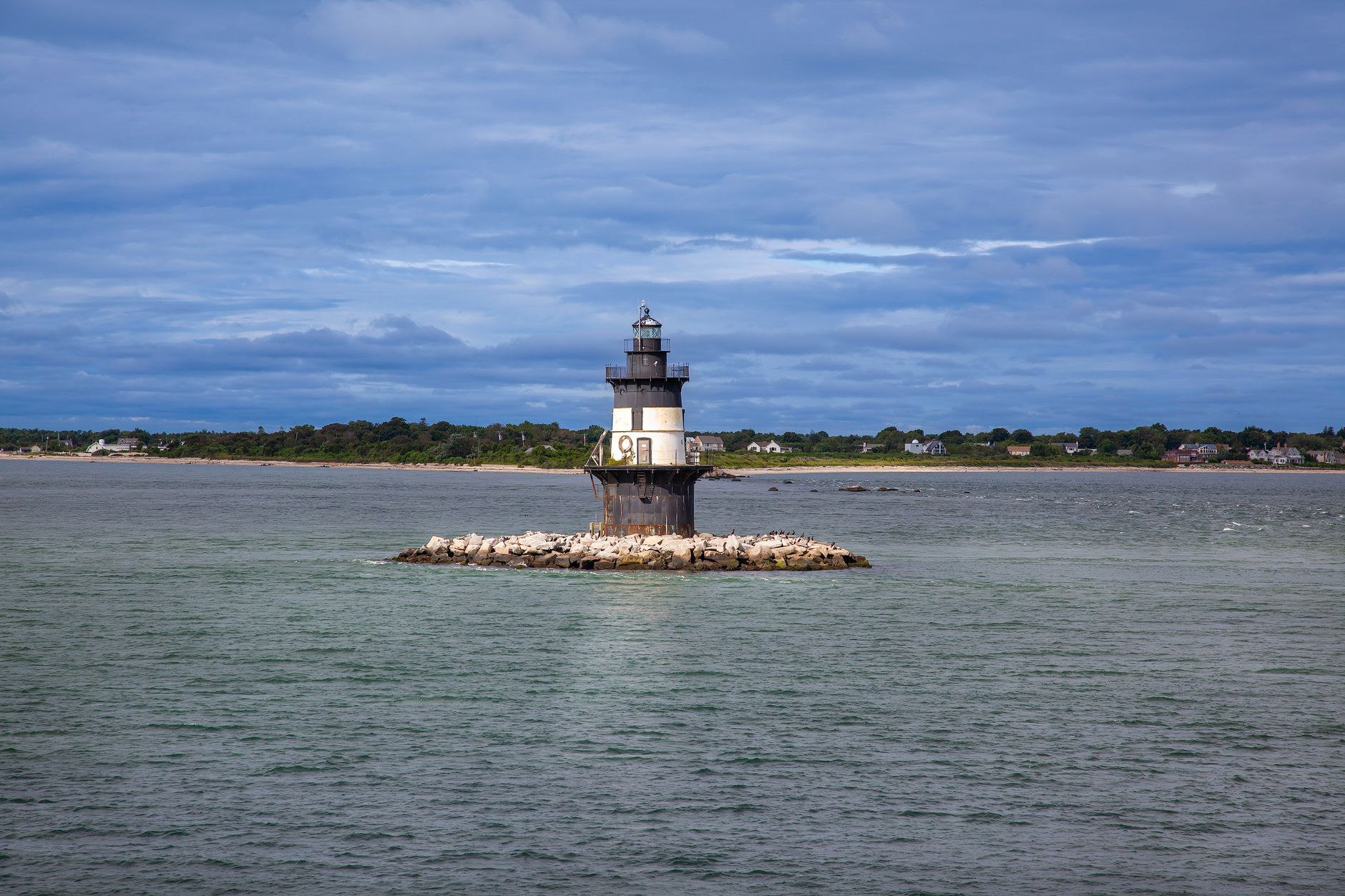 Serene view of Orient Point Lighthouse on a rocky islet in New York, surrounded by calm sea and distant shoreline.