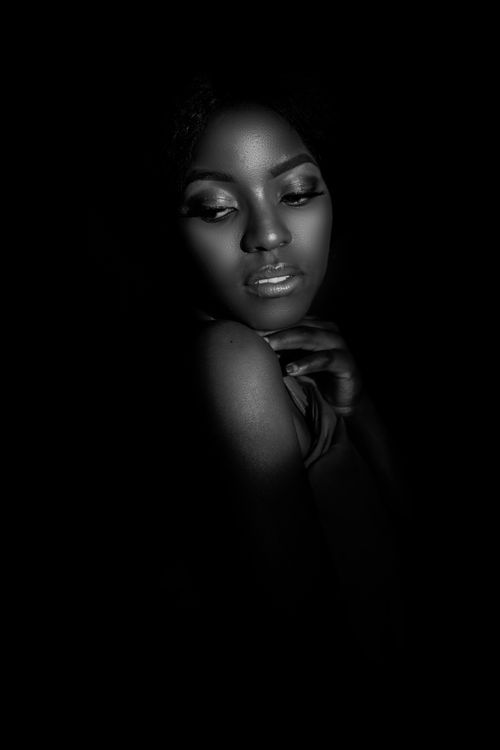 Free Black and white portrait of a young African woman with dramatic lighting casting shadows on her face. Stock Photo