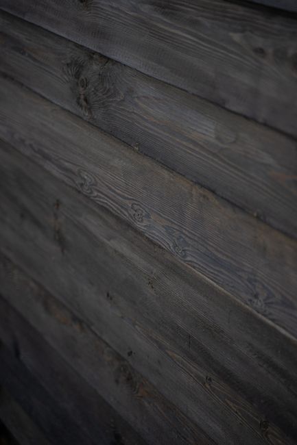 Close-up of a dark wooden wall with a rough, rustic texture and weathered appearance.