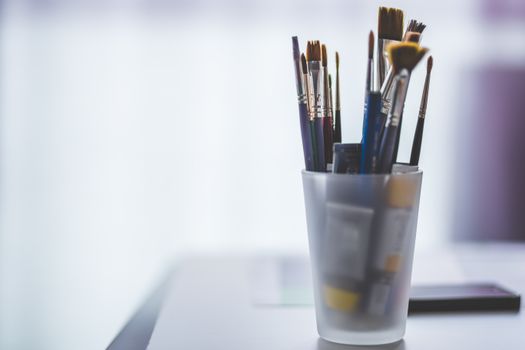 An assortment of paint brushes in a translucent cup, ideal for artists.