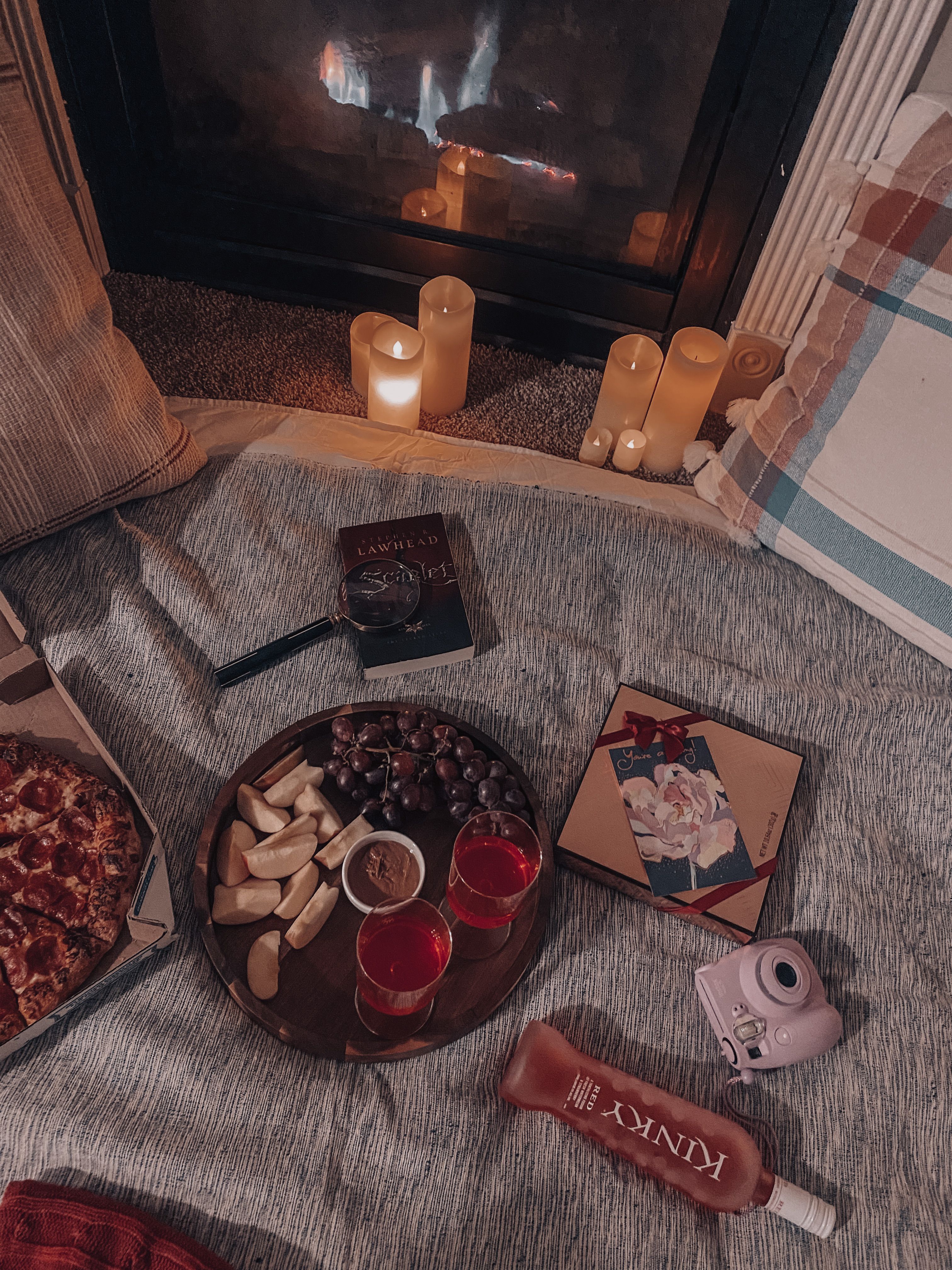 A relaxing setup by the fireplace with snacks, books, and candles for a cozy evening indoors.