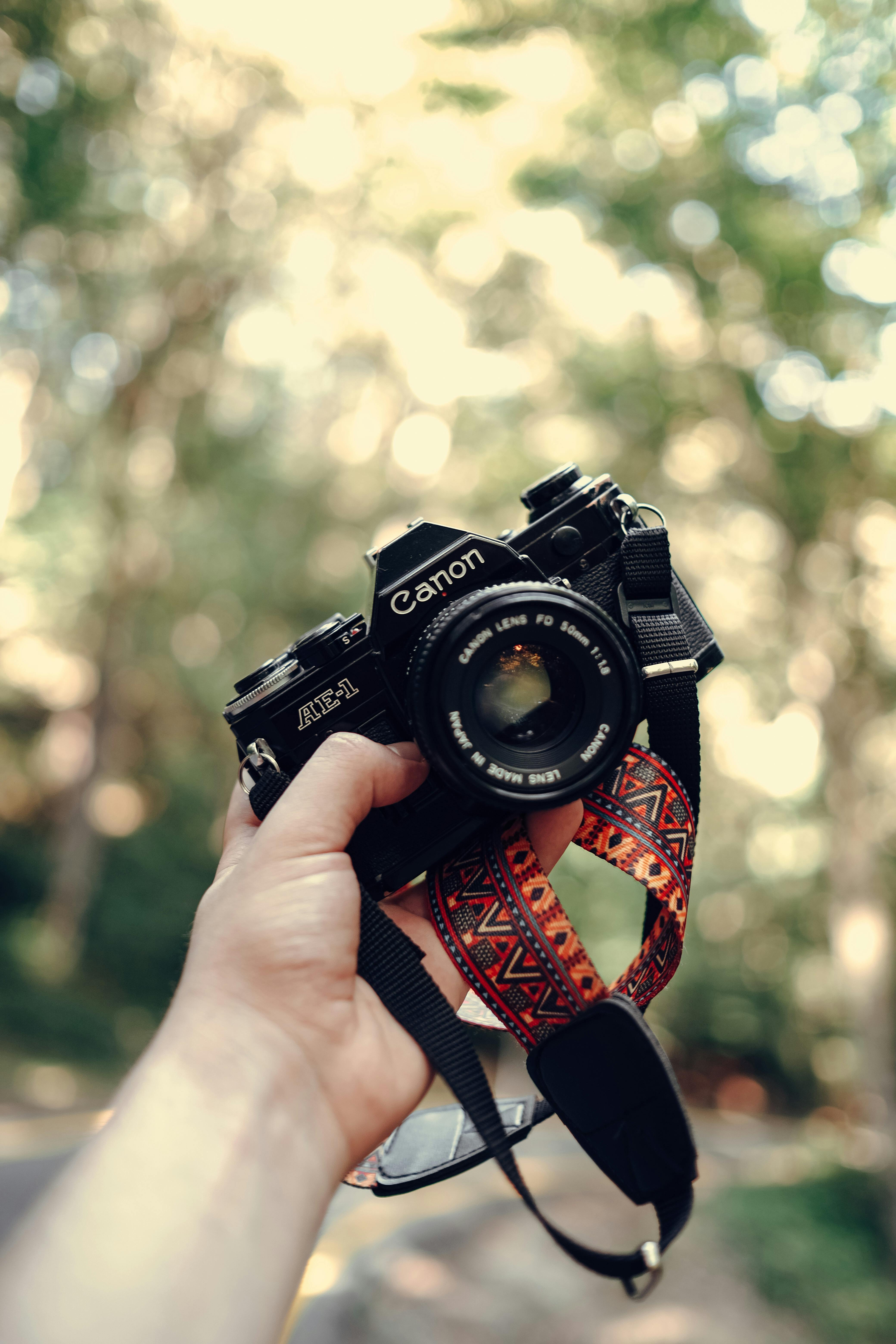 Free A person holding a vintage film camera with a custom strap in an outdoor setting. Stock Photo