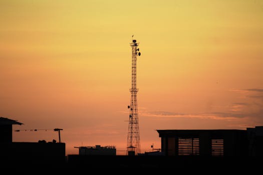 Urban landscape silhouette featuring a communication tower against a vibrant sunset sky.