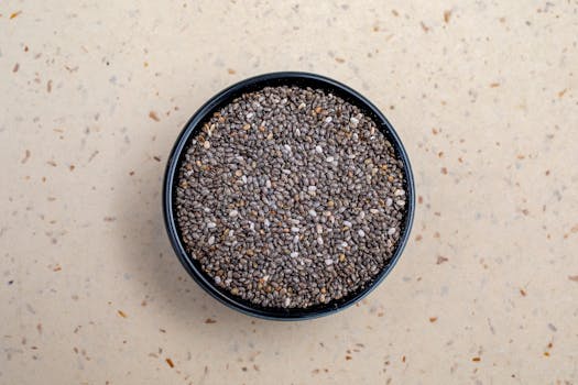 A close-up image of chia seeds in a black bowl on a speckled beige background.