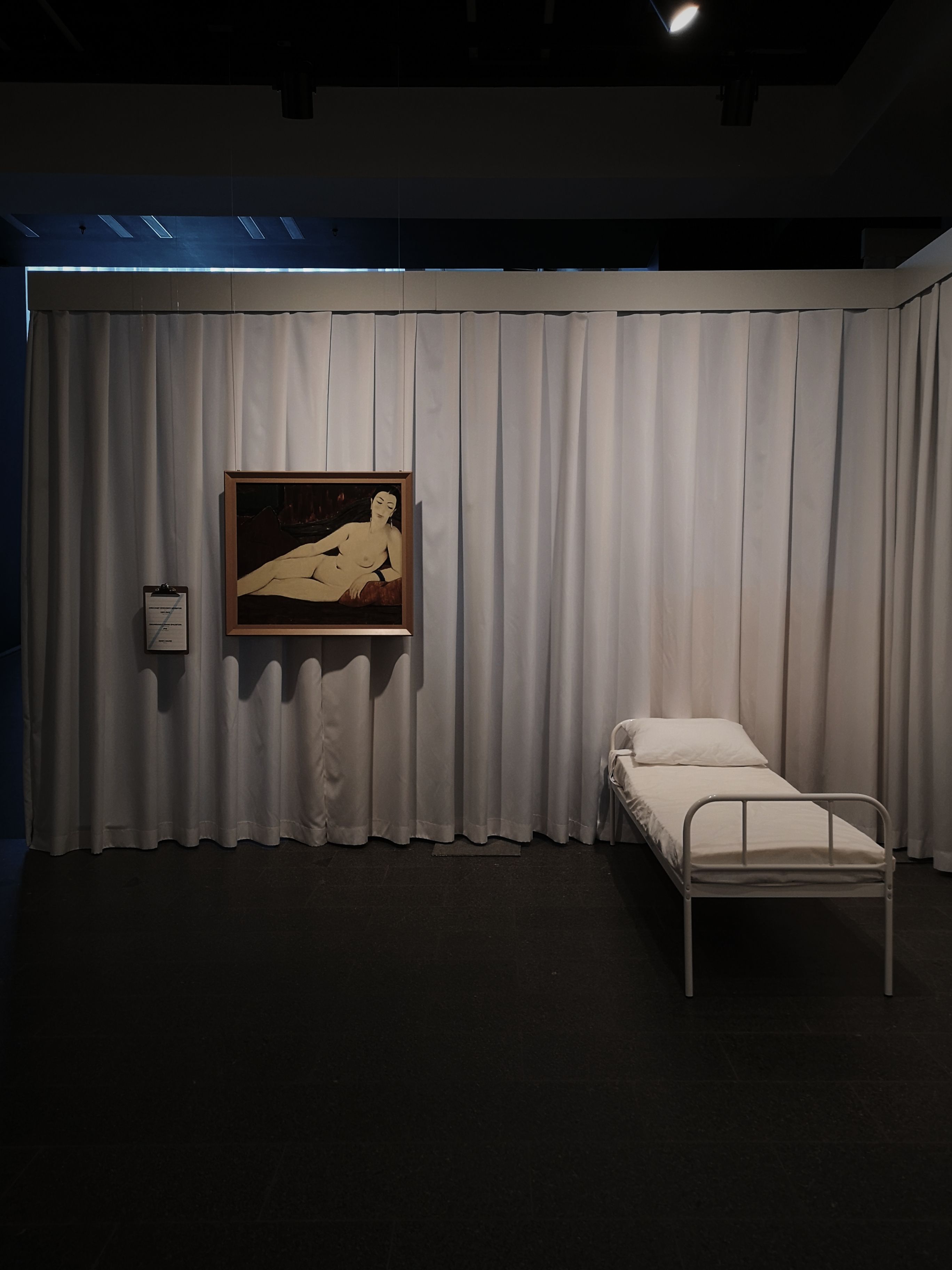Minimalist gallery setup features a bed and painting exhibition.