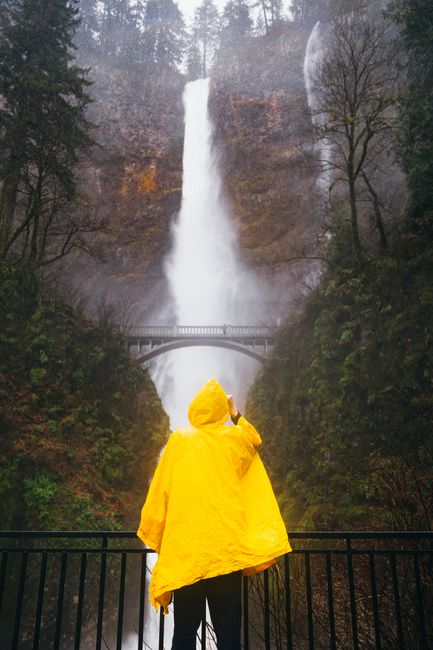 A person in a yellow raincoat stands in awe before the majestic Multnomah Falls in Oregon.