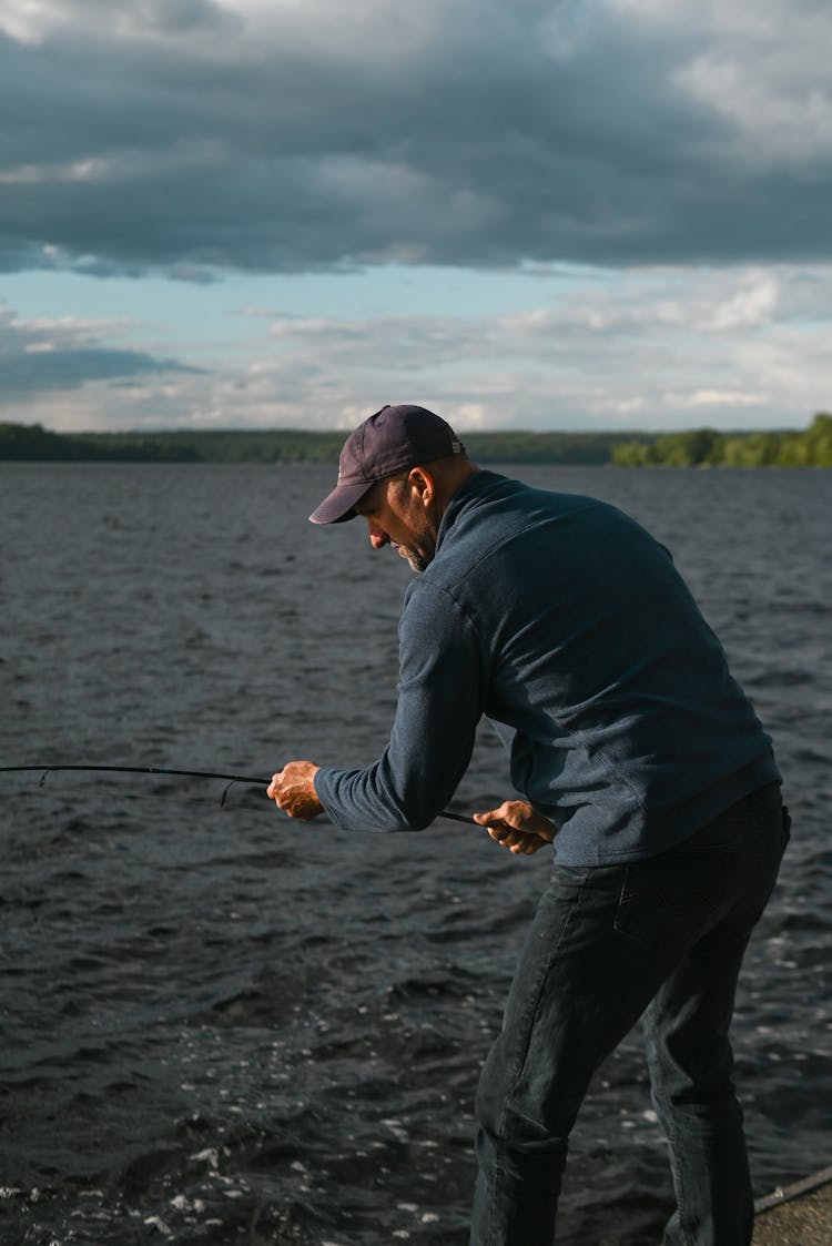 A Man Holding A Fishing Rod While Standing On A Dock