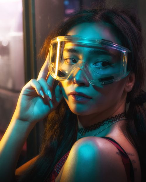 Free Stylish woman in goggles poses with colorful lighting indoors. Stock Photo