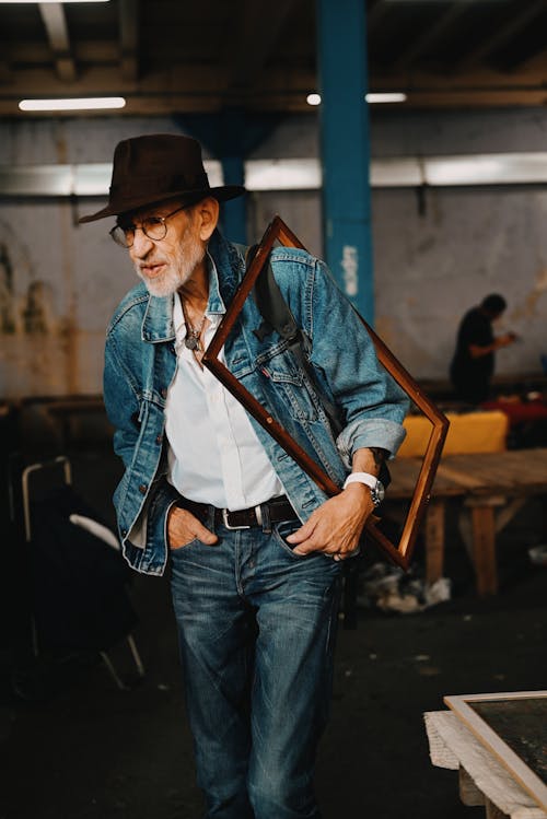 An Elderly Man in Denim Jacket Carrying a Wooden Frame
