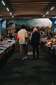 Two men walk through a busy indoor market surrounded by various stalls and goods.