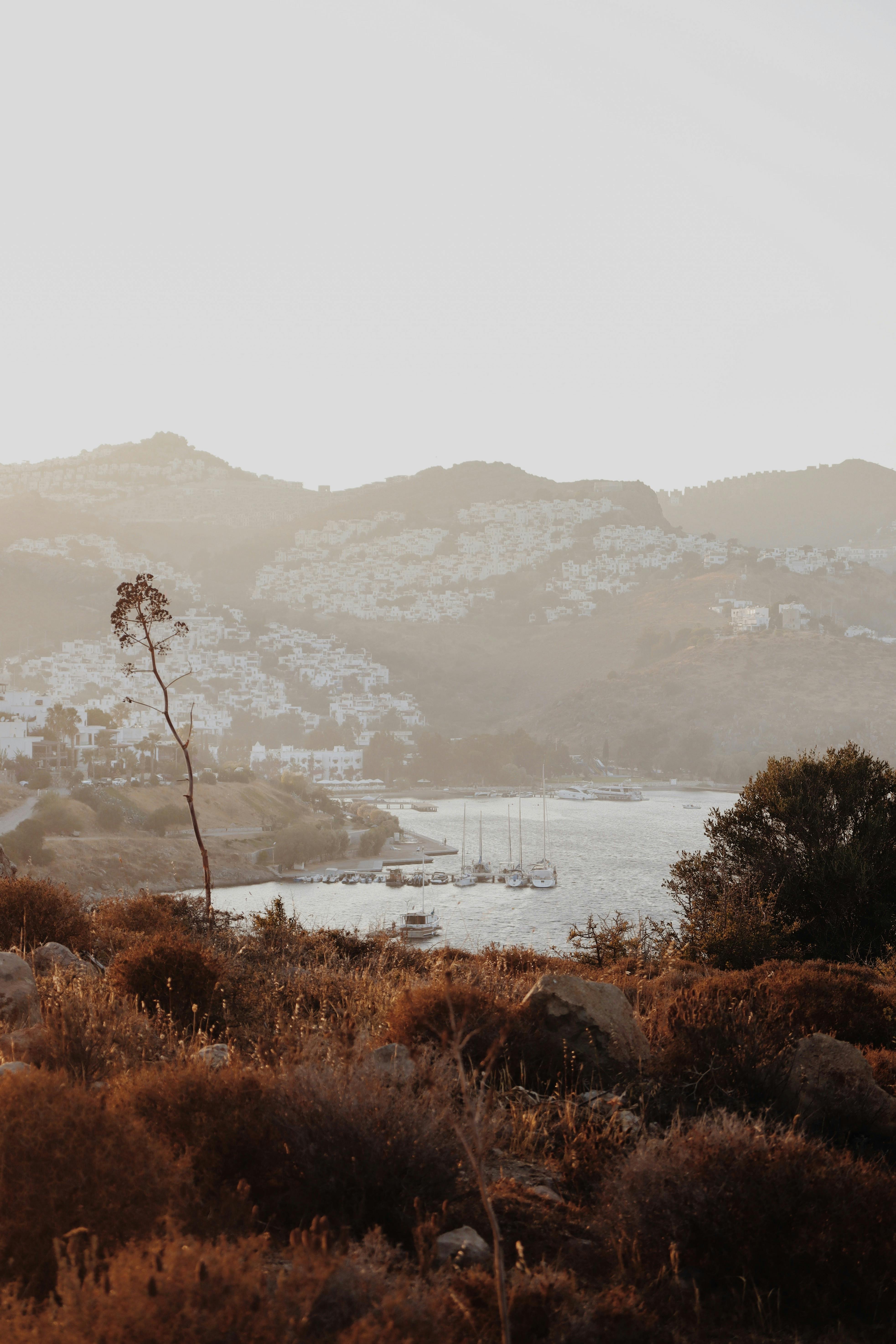 A tranquil marina nestled between mountains at dusk, featuring boats and autumn foliage.