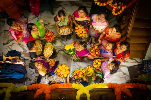 Overhead view of women in colorful sarees holding fruit platters during a festive celebration.