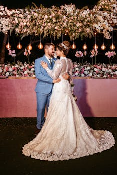 Bride and groom embrace under floral arch in an outdoor evening wedding ceremony.