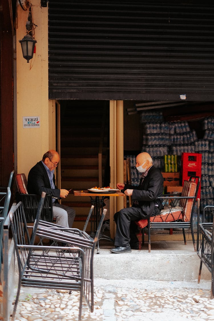 A Man In Black Jacket Sitting At A Table Across A Person Wearing Face Mask