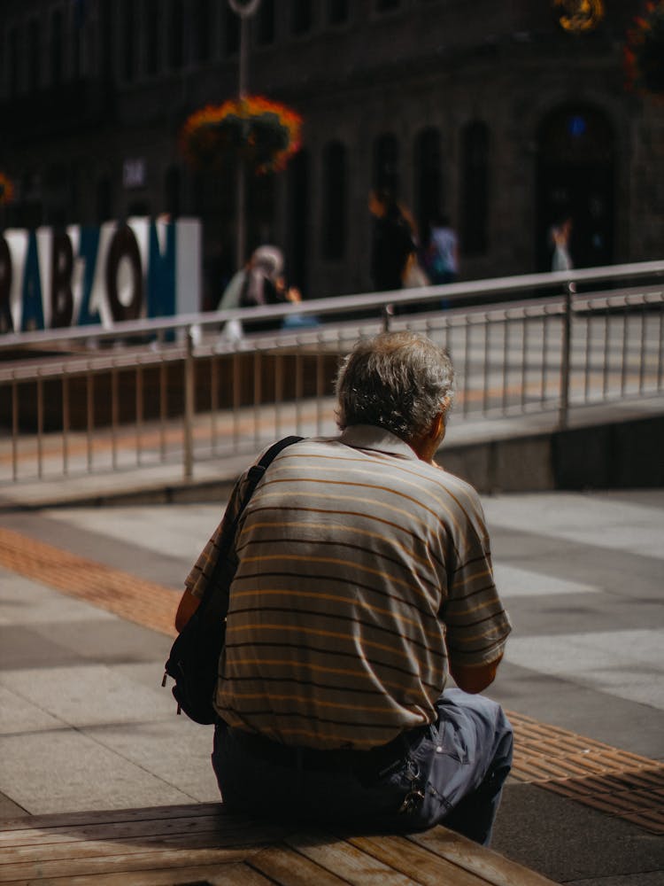 Old Man Sitting On Bench On City Square