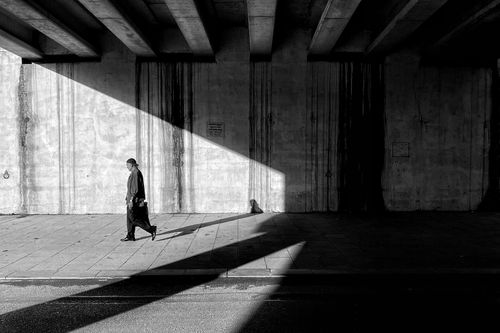 Free A solitary pedestrian walks under an urban bridge casting dramatic shadows. Stock Photo