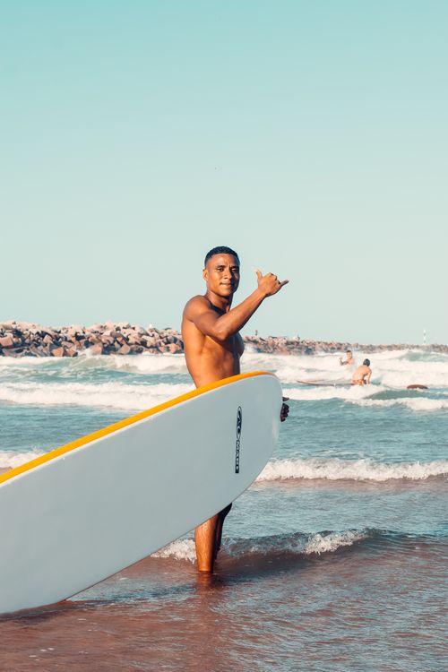 Free Man with surfboard making shaka sign at Fortaleza beach, Brazil. Perfect day for surfing and ocean fun. Stock Photo