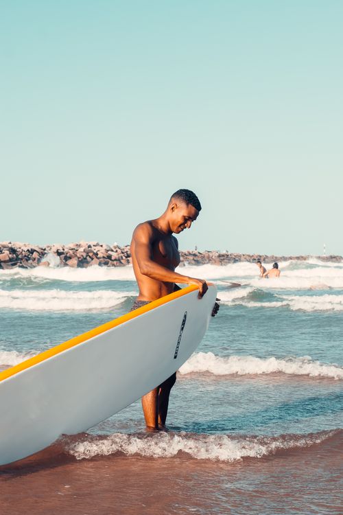 Free Shirtless man with surfboard standing on a sunny beach in Fortaleza, Brazil. Stock Photo