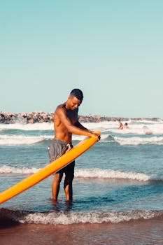 A man prepares his surfboard for water sports on a tropical beach in Fortaleza, Brazil.