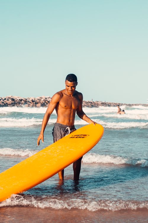 Free Surfer holding a yellow surfboard on the sunny beach in Fortaleza, Brazil. Stock Photo