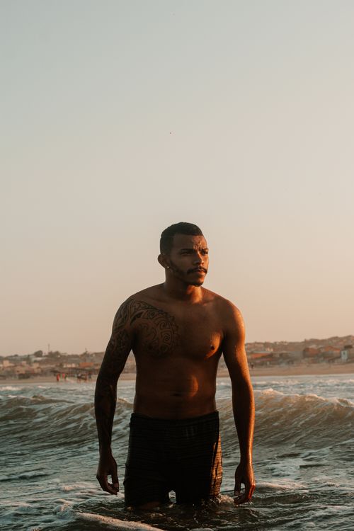 Free Portrait of a shirtless man with tattoos standing in the ocean during sunset, exuding a calm and introspective vibe. Stock Photo