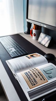 A modern workspace featuring a book open on typography, with a sleek monitor, keyboard, and tablet.