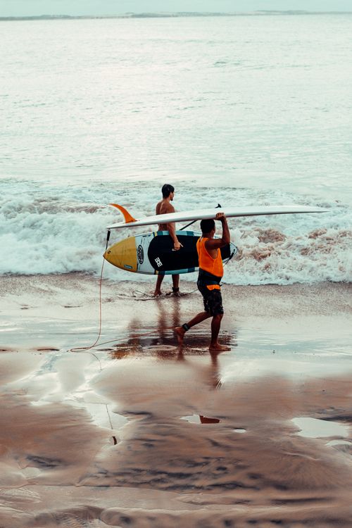 Free Two surfers carrying boards walk along the sandy beach of Paracuru, Brazil, on a bright day. Stock Photo