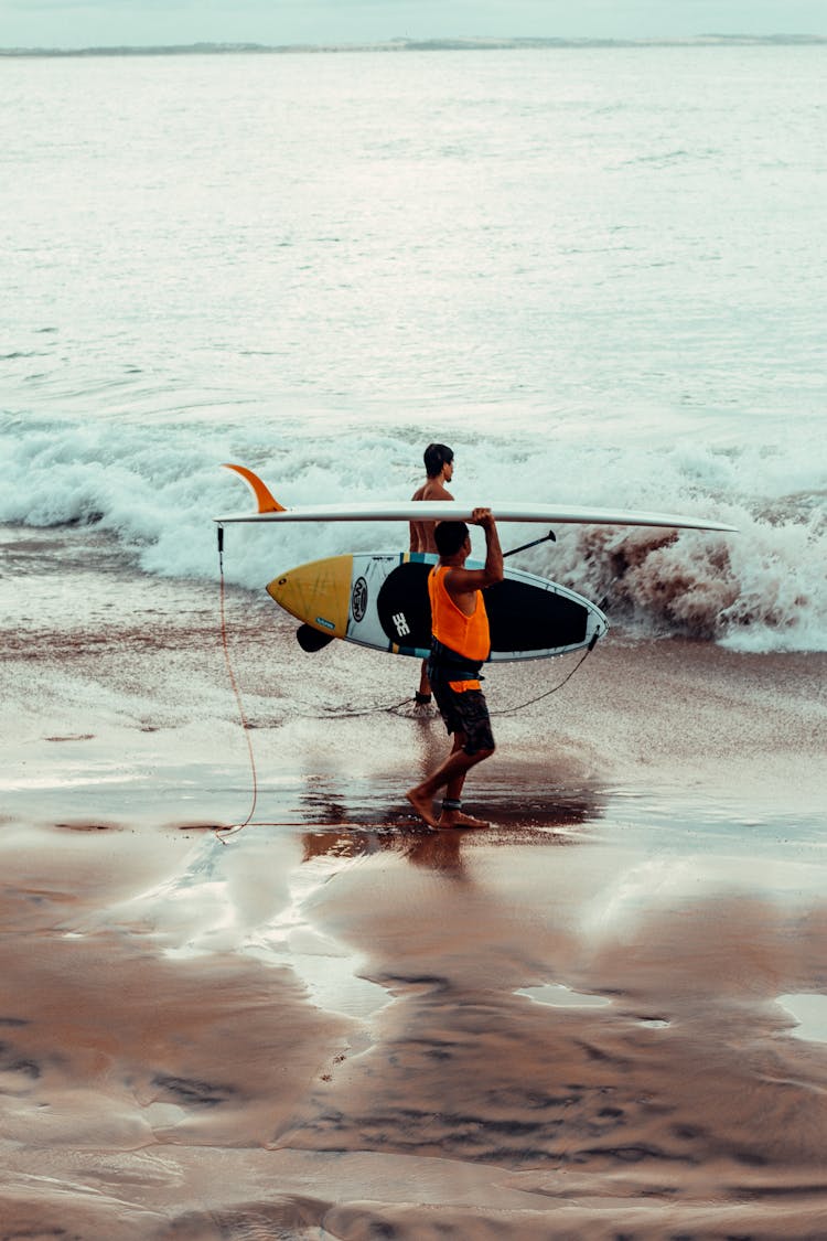 Two Men Carrying Surfboards Walking On Beach