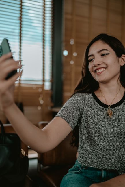 Young woman smiling while taking a selfie with her phone inside, capturing a joyful moment.