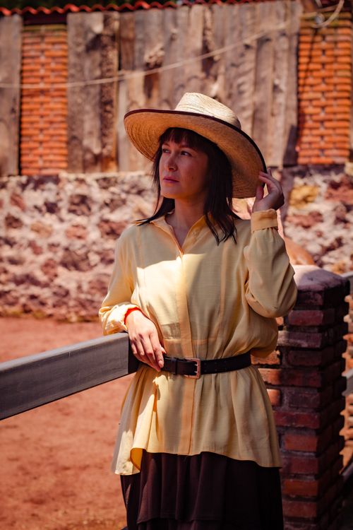 Free Woman leaning on a fence outdoors wearing a straw hat and yellow dress with brown belt. Stock Photo